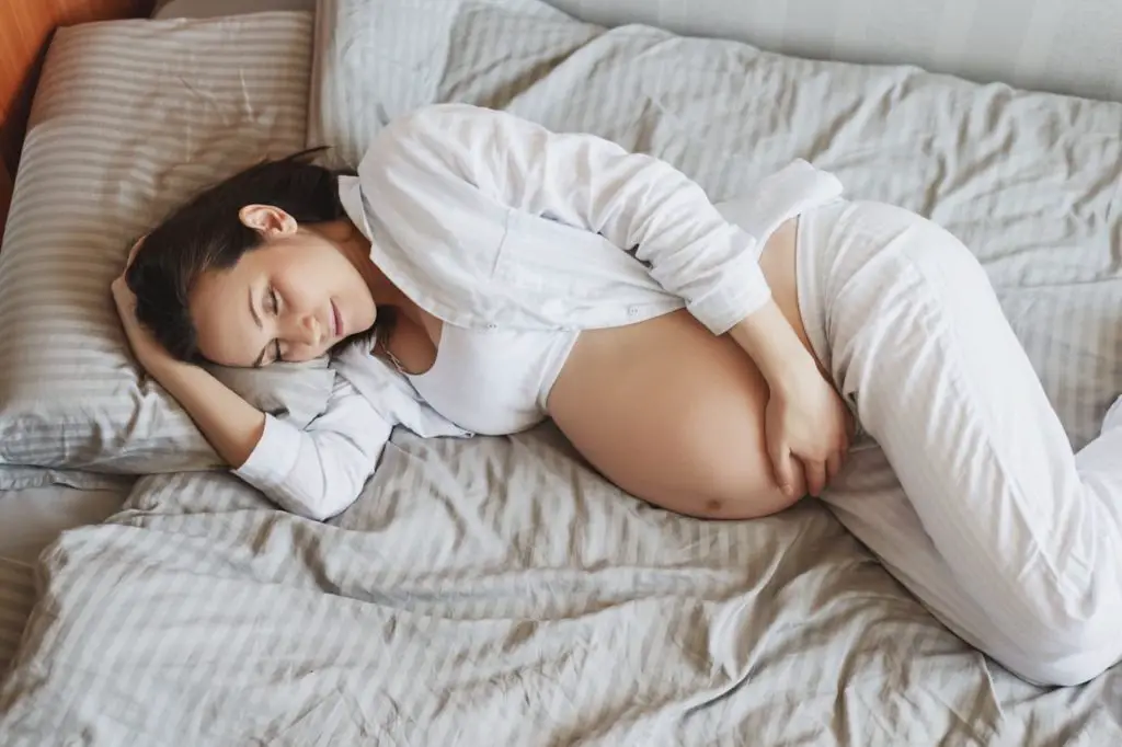 Young pregnant woman lying on bed hugging her tummy - Carnivore Diet During Pregnancy