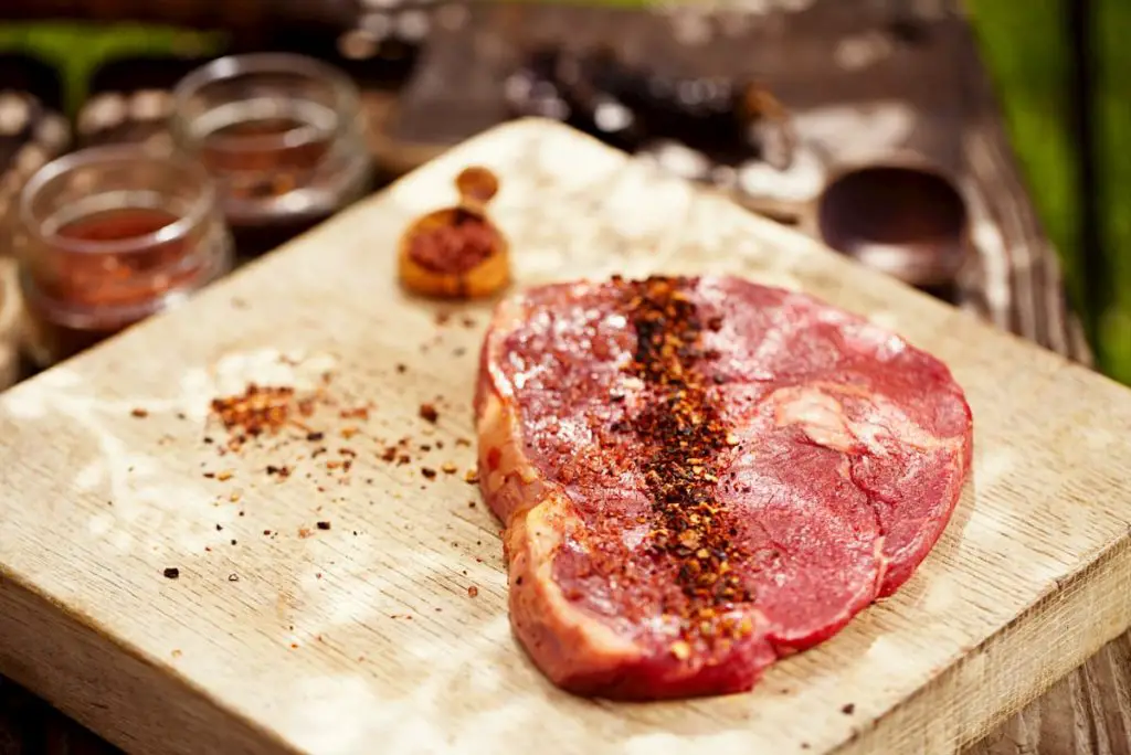 Chipotle flakes chilli spice with bbq raw beef steak on wooden - meal prep carnivore diet